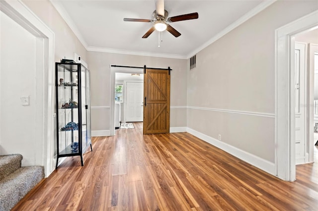 unfurnished room featuring crown molding, wood-type flooring, a barn door, and ceiling fan