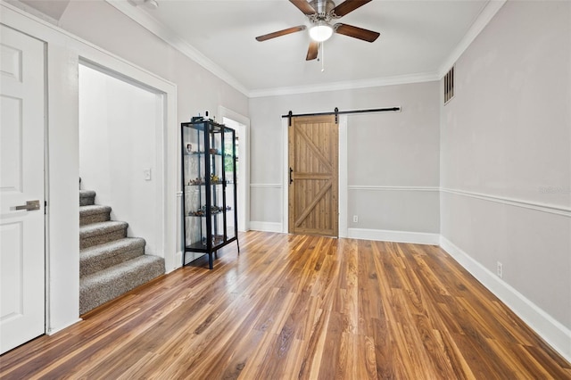 spare room featuring crown molding, wood-type flooring, a barn door, and ceiling fan