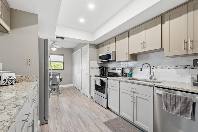 kitchen with sink, ceiling fan, stainless steel appliances, tasteful backsplash, and light stone counters