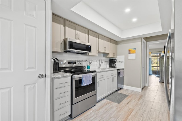 kitchen featuring appliances with stainless steel finishes, sink, decorative backsplash, and a tray ceiling