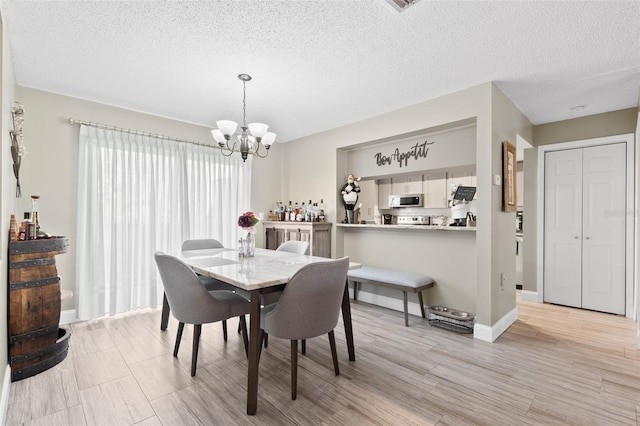 dining room featuring a notable chandelier, light hardwood / wood-style flooring, and a textured ceiling