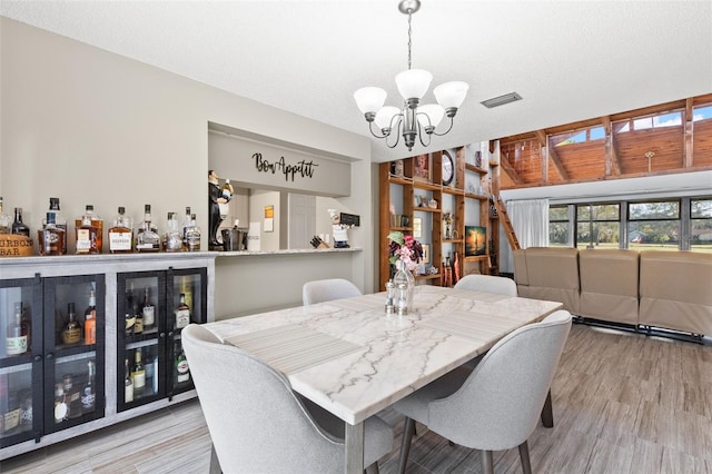 dining area with an inviting chandelier, bar, and light hardwood / wood-style flooring