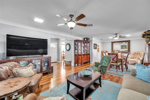 living room with ceiling fan, brick wall, and light wood-type flooring