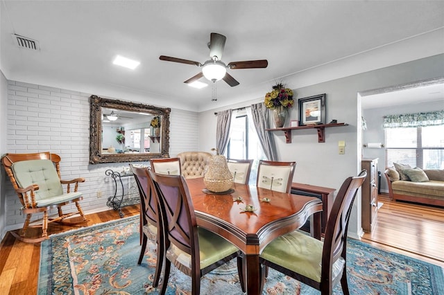 dining space featuring ceiling fan, brick wall, and hardwood / wood-style floors