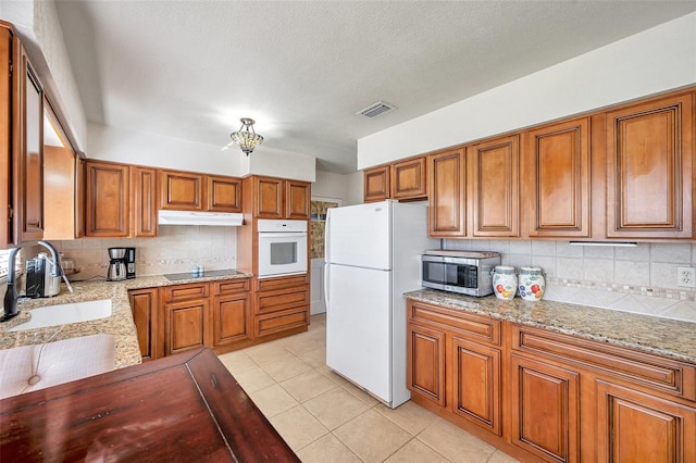 kitchen with tasteful backsplash, sink, light tile patterned floors, light stone countertops, and white appliances