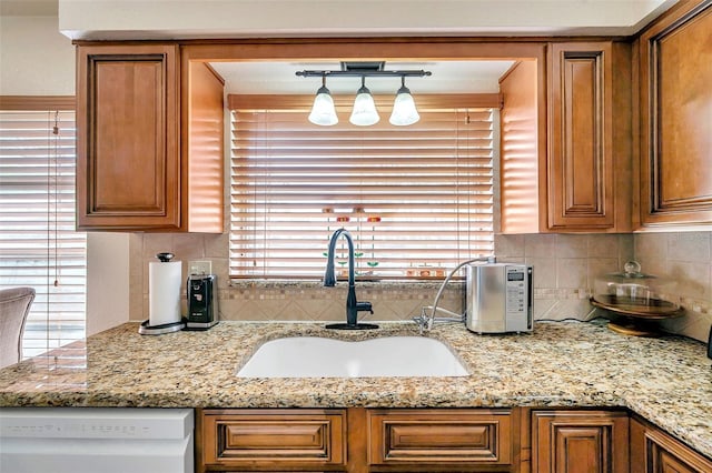 kitchen with white dishwasher, sink, light stone counters, and plenty of natural light