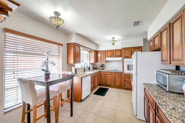 kitchen with white appliances, light stone countertops, a textured ceiling, and light tile patterned flooring