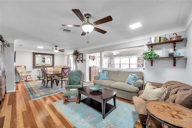 living room with light wood-style flooring, visible vents, brick wall, and ceiling fan