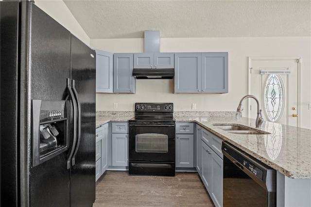 kitchen featuring sink, dark wood-type flooring, light stone counters, black appliances, and a textured ceiling