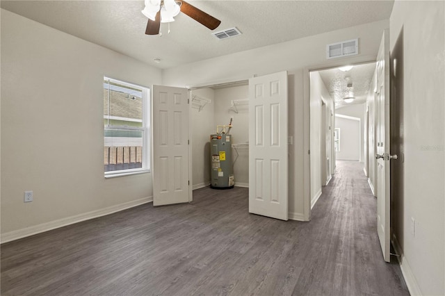 unfurnished bedroom with dark wood-type flooring, a textured ceiling, a closet, ceiling fan, and water heater