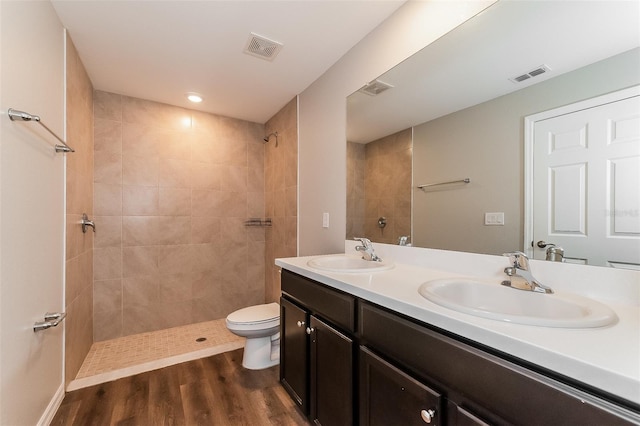 bathroom with wood-type flooring, a tile shower, vanity, and toilet