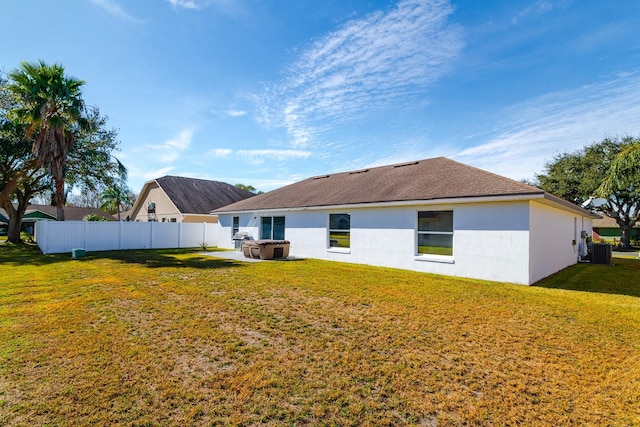 rear view of house with central AC, a jacuzzi, and a lawn