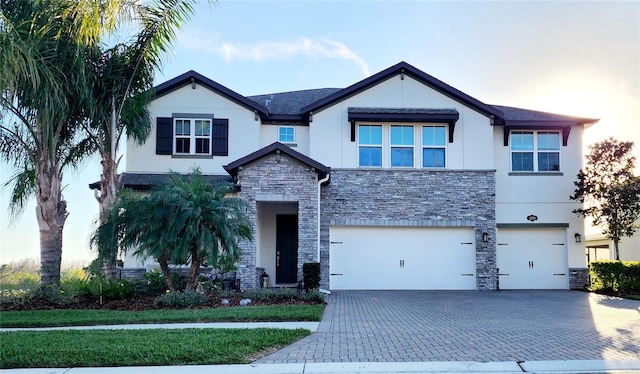 view of front of house with decorative driveway, stone siding, an attached garage, and stucco siding