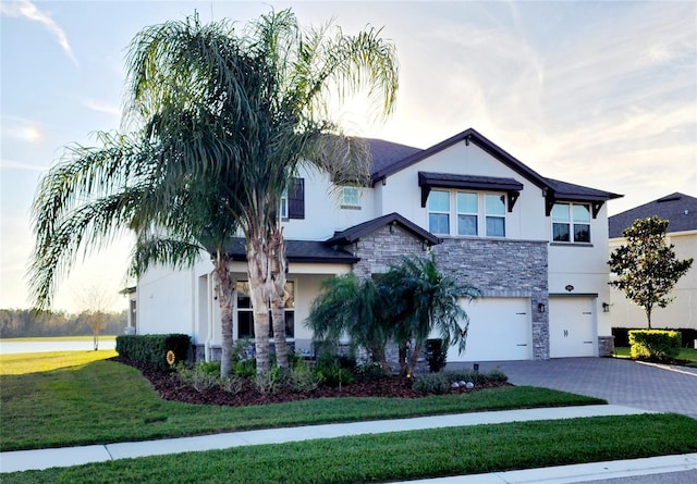 view of front of house with a garage, stone siding, decorative driveway, a front yard, and stucco siding