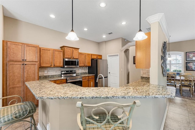 kitchen featuring appliances with stainless steel finishes, a kitchen bar, decorative backsplash, hanging light fixtures, and kitchen peninsula