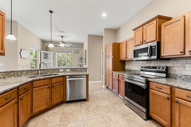 kitchen featuring sink, appliances with stainless steel finishes, light stone counters, tasteful backsplash, and decorative light fixtures