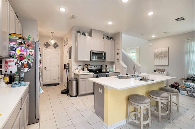 kitchen featuring sink, decorative light fixtures, appliances with stainless steel finishes, a kitchen breakfast bar, and an island with sink