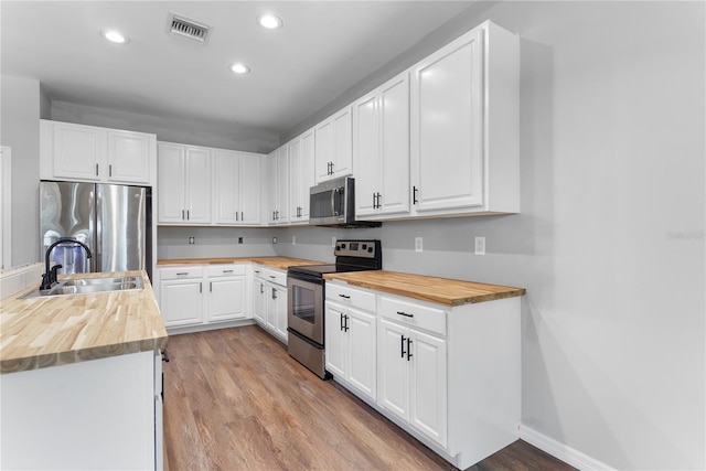 kitchen featuring sink, butcher block countertops, light hardwood / wood-style flooring, stainless steel appliances, and white cabinets