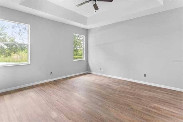 empty room with hardwood / wood-style flooring, a raised ceiling, and ceiling fan