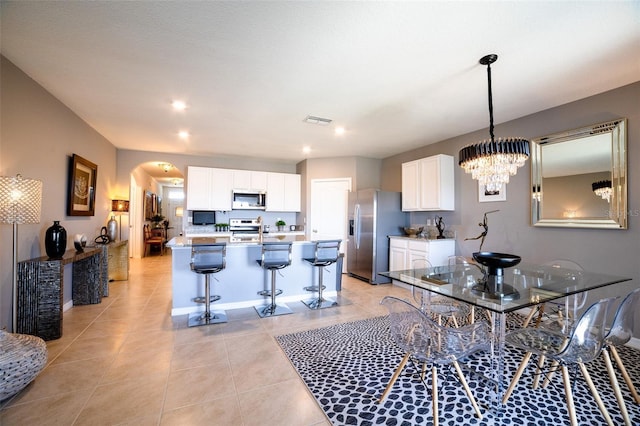 kitchen with appliances with stainless steel finishes, white cabinetry, a kitchen breakfast bar, a kitchen island with sink, and light tile patterned floors