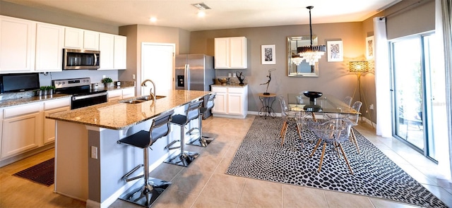 kitchen featuring sink, appliances with stainless steel finishes, a kitchen island with sink, white cabinets, and decorative light fixtures