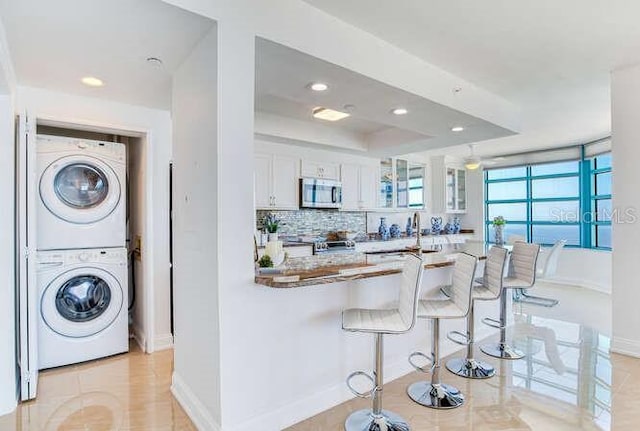 kitchen featuring white cabinetry, a kitchen breakfast bar, stacked washer and clothes dryer, a tray ceiling, and stainless steel appliances