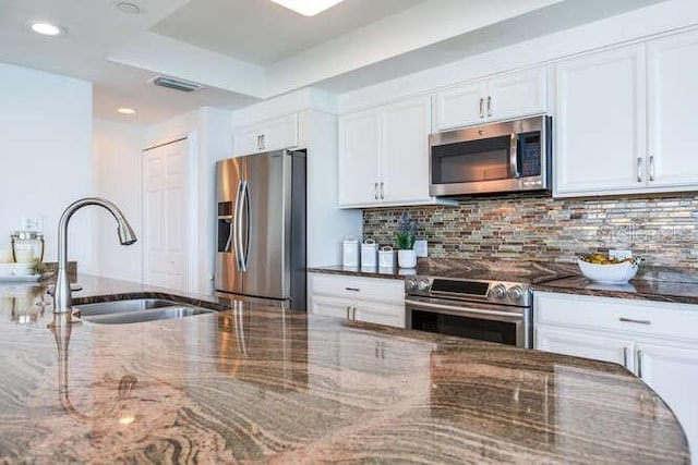 kitchen with white cabinets, stainless steel appliances, sink, and dark stone countertops