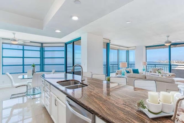 kitchen with sink, white cabinetry, a water view, stainless steel dishwasher, and dark stone counters