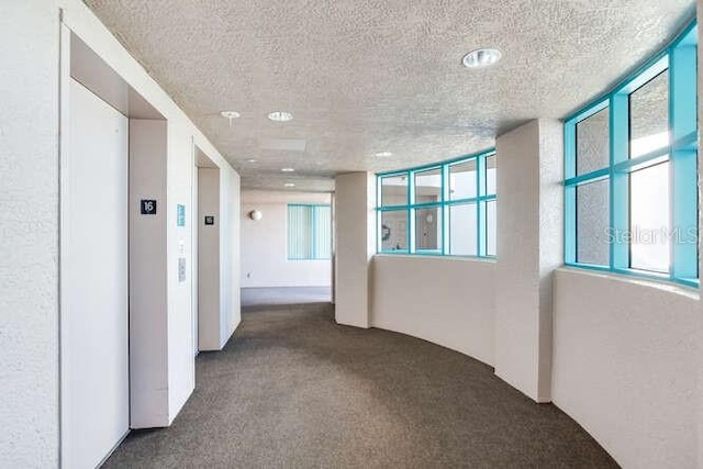 corridor featuring dark colored carpet, elevator, and a textured ceiling