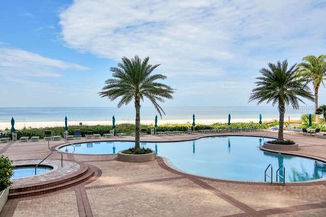 view of swimming pool with a hot tub, a water view, and a patio area