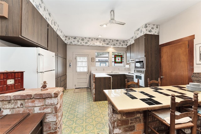 kitchen featuring ceiling fan, dark brown cabinets, white appliances, and kitchen peninsula