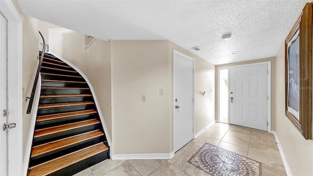 foyer featuring stairway, baseboards, a textured ceiling, and light tile patterned floors