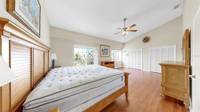 bedroom with wood finished floors, multiple closets, a ceiling fan, high vaulted ceiling, and baseboards