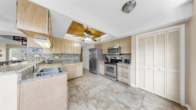 kitchen with appliances with stainless steel finishes, a sink, a raised ceiling, and light brown cabinets