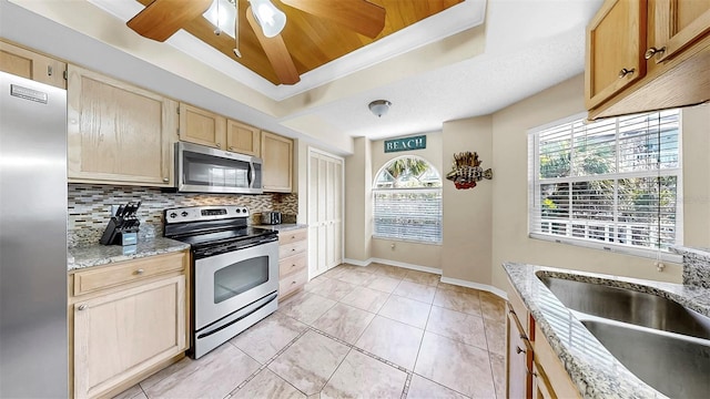 kitchen with appliances with stainless steel finishes, a sink, light brown cabinetry, decorative backsplash, and a tray ceiling
