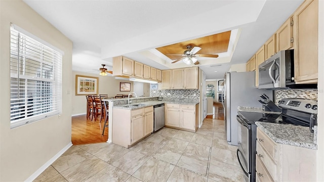kitchen featuring appliances with stainless steel finishes, a raised ceiling, ceiling fan, and light brown cabinetry