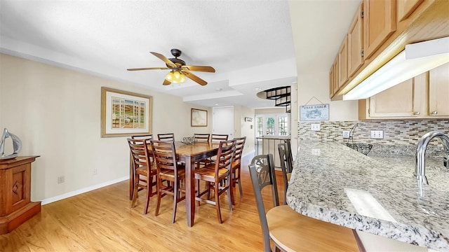dining room with light wood-type flooring, a ceiling fan, and baseboards