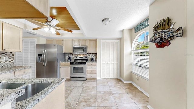 kitchen with stainless steel appliances, backsplash, a sink, and a ceiling fan