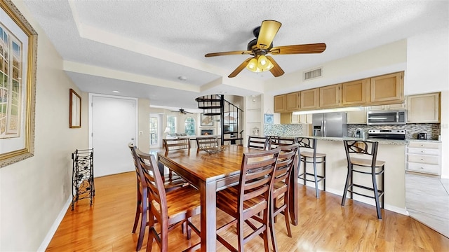 dining space with a ceiling fan, light wood-style floors, a textured ceiling, and baseboards