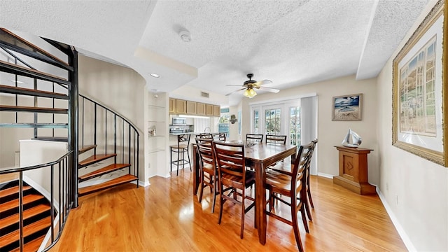 dining area with a textured ceiling, light wood-type flooring, ceiling fan, baseboards, and stairway