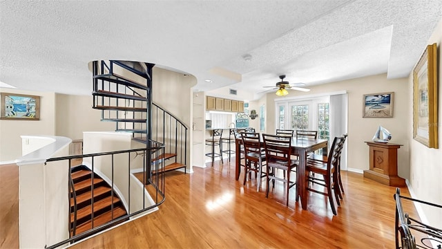dining area with a textured ceiling, light wood-type flooring, ceiling fan, baseboards, and stairway