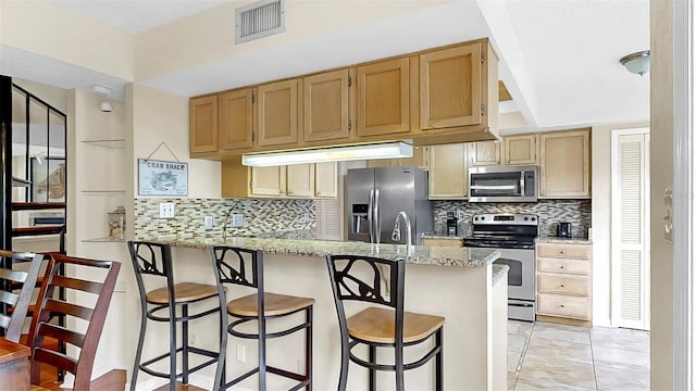 kitchen featuring appliances with stainless steel finishes, a peninsula, backsplash, and a breakfast bar