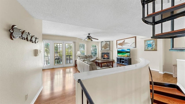 interior space with a textured ceiling, light wood-style floors, ceiling fan, a lit fireplace, and baseboards