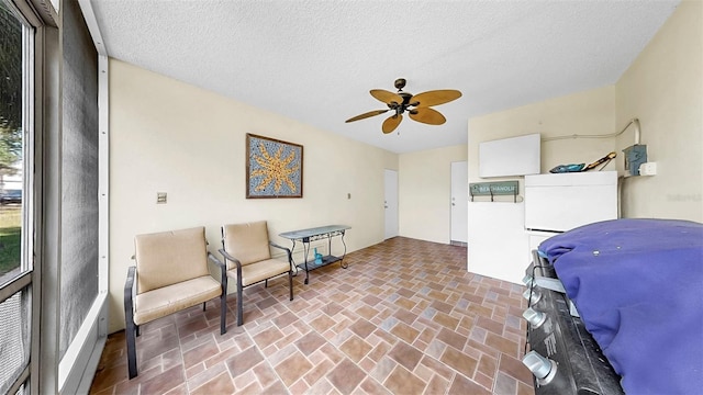 living area featuring a ceiling fan, brick patterned floors, and a textured ceiling