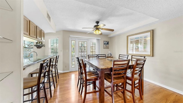 dining space with a textured ceiling, light wood-type flooring, a ceiling fan, and baseboards