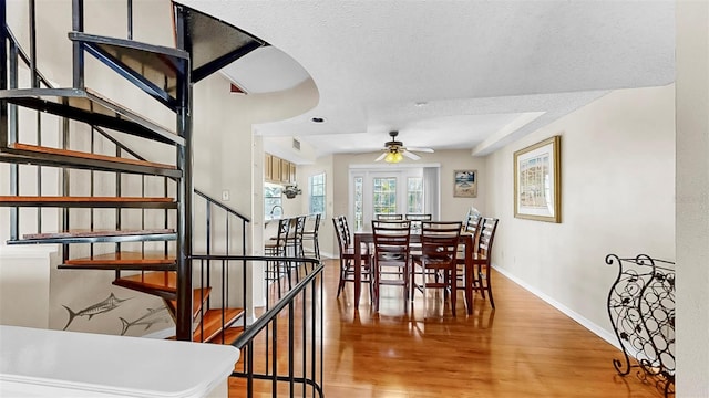 dining room featuring a ceiling fan, stairway, light wood-style floors, baseboards, and a textured ceiling