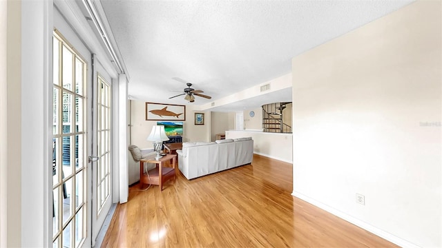 living area with light wood-style floors, ceiling fan, baseboards, and a textured ceiling