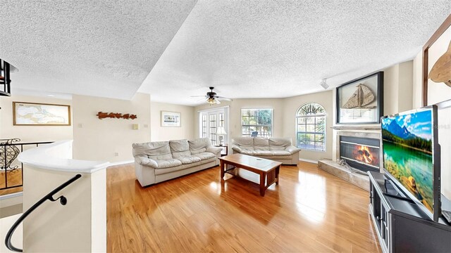 living room with light wood-style flooring, a textured ceiling, a ceiling fan, a glass covered fireplace, and baseboards