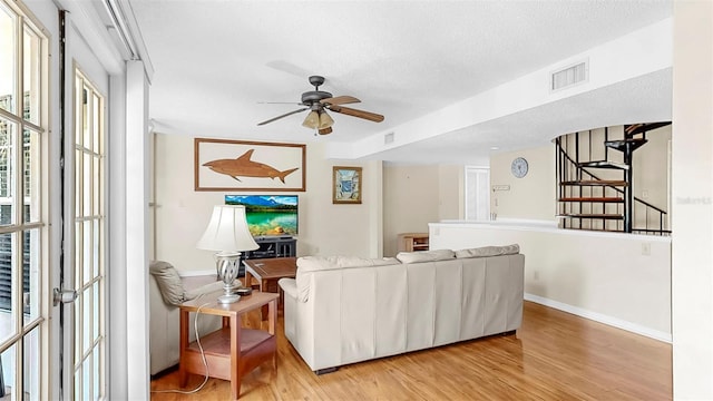 living area with light wood finished floors, ceiling fan, baseboards, a textured ceiling, and stairs