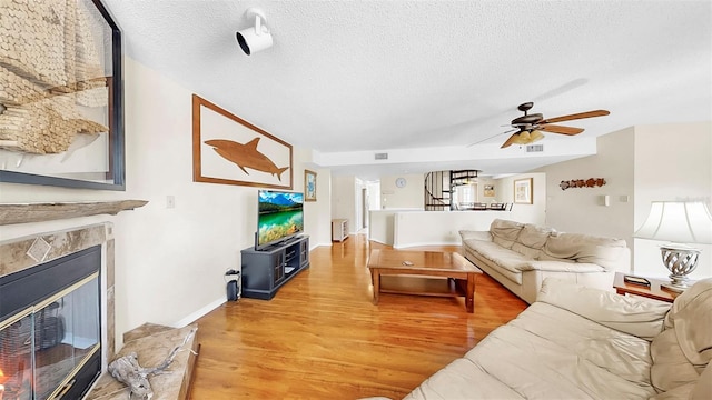 living room featuring a textured ceiling, light wood-type flooring, stairs, a ceiling fan, and a high end fireplace